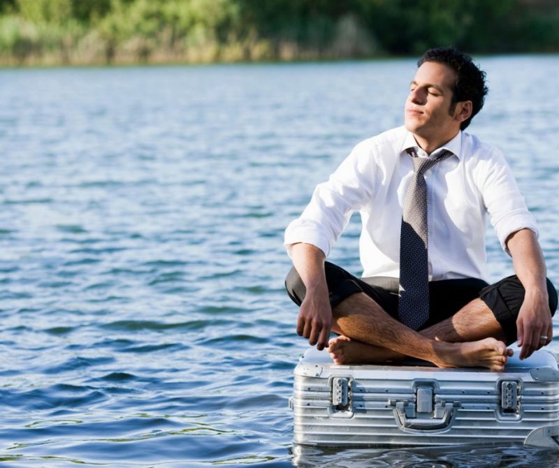Homme avec une cravate assis sur une valise qui flotte sur l'eau | Dr François Auger Chiropraticien - Chiropratique Québec, Chiro Nord, Stoneham, NDL, Lac Saint-Charles