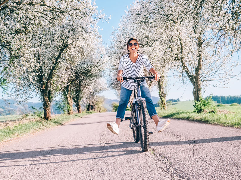 Femme heureuse en vélo sous les arbres en fleurs. | Dr François Auger Chiropraticien - Chiropratique Québec, Chiro Nord, Stoneham, NDL, Lac Saint-Charles